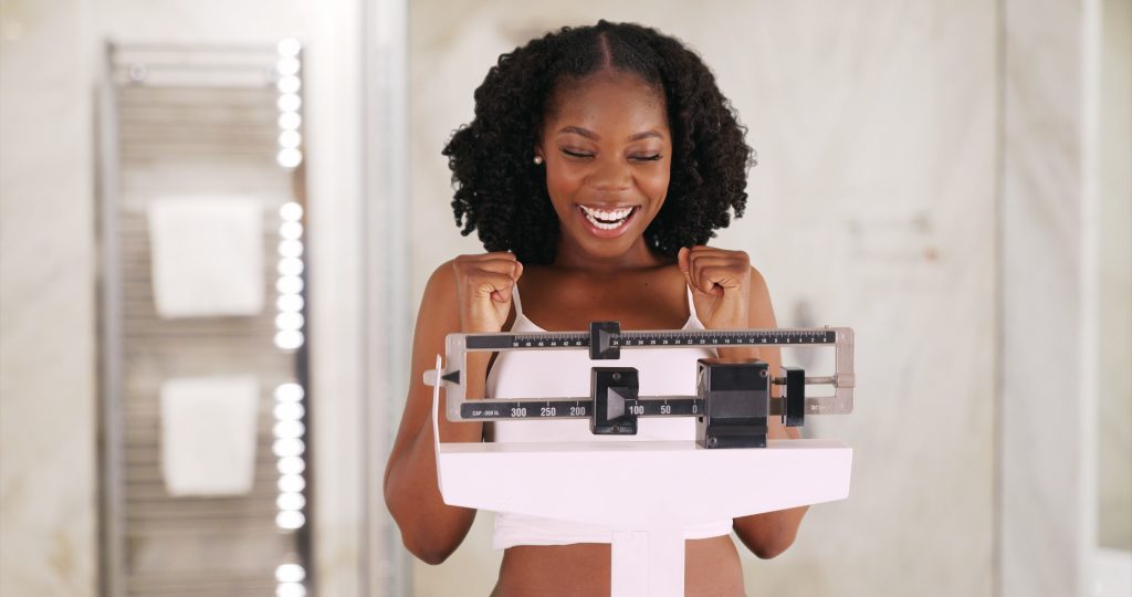 A woman is smiling while standing on a scale.