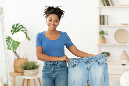 A woman holding up her jeans and smiling.