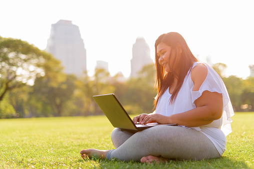 A woman sitting on the grass using her laptop.