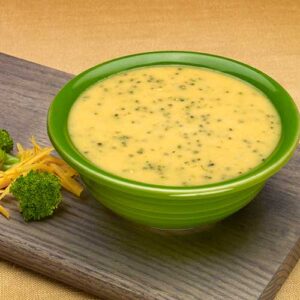 A bowl of broccoli soup on top of a wooden board.