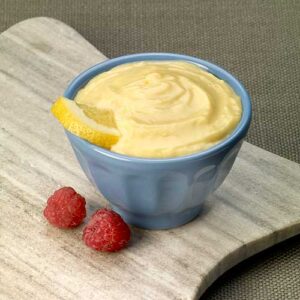 A bowl of yellow pudding with raspberries on the side.