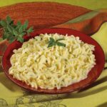 A red bowl of macaroni and cheese on top of a table.