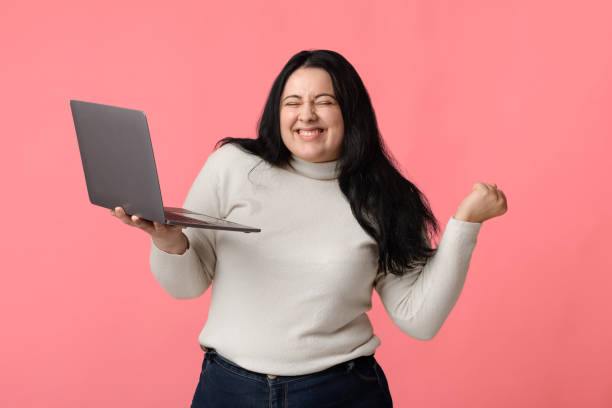 A woman holding her laptop and celebrating with her arms raised.